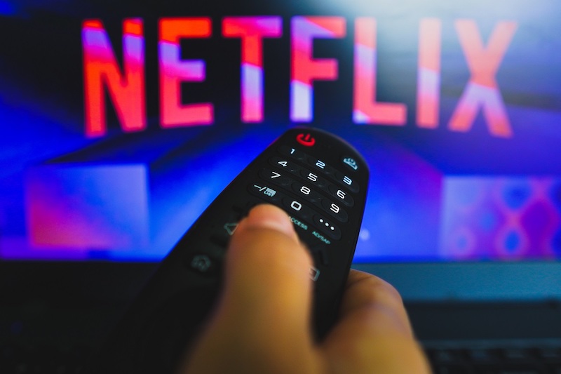 May 10, 2022, Brazil. In this photo illustration a close up of a hand holding a TV remote control seen in front of the Netflix logo.